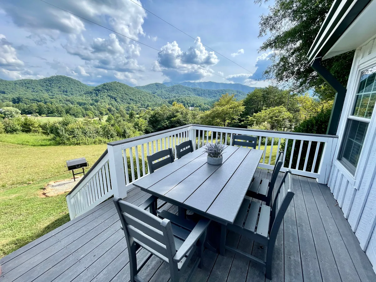This image captures an inviting wooden dining table set on a spacious outdoor deck, framed by a stunning mountain view and complemented by a leafy potted plant. The natural setting suggests ample space for friends and family to gather and dine al fresco while soaking in the scenery.