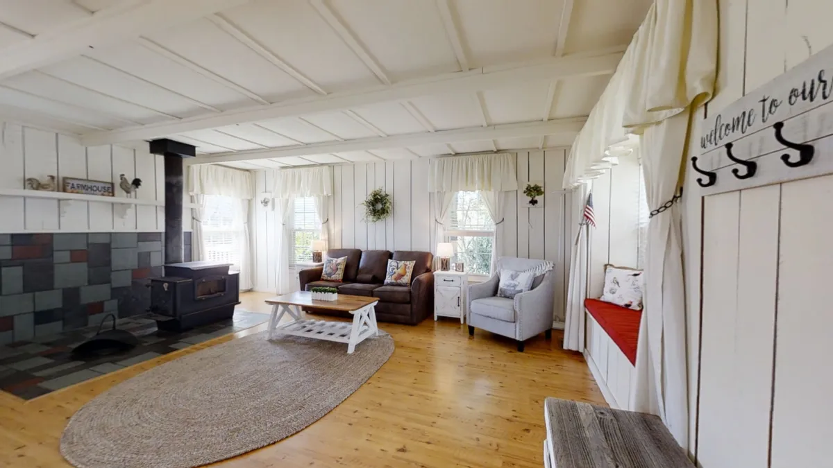 A cozy living room with a brown sofa, blue armchair, coffee table, and a wood stove, with a view out the windows to the mountain scenery. The space feels intimate and inviting, encouraging conversation and relaxation.