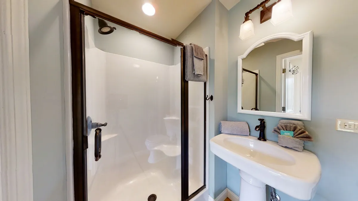 A modern bathroom featuring a walk-in glass shower with a bench seat, a pedestal sink, a well-lit mirror, and contemporary fixtures. The space is designed for both functionality and relaxation.
