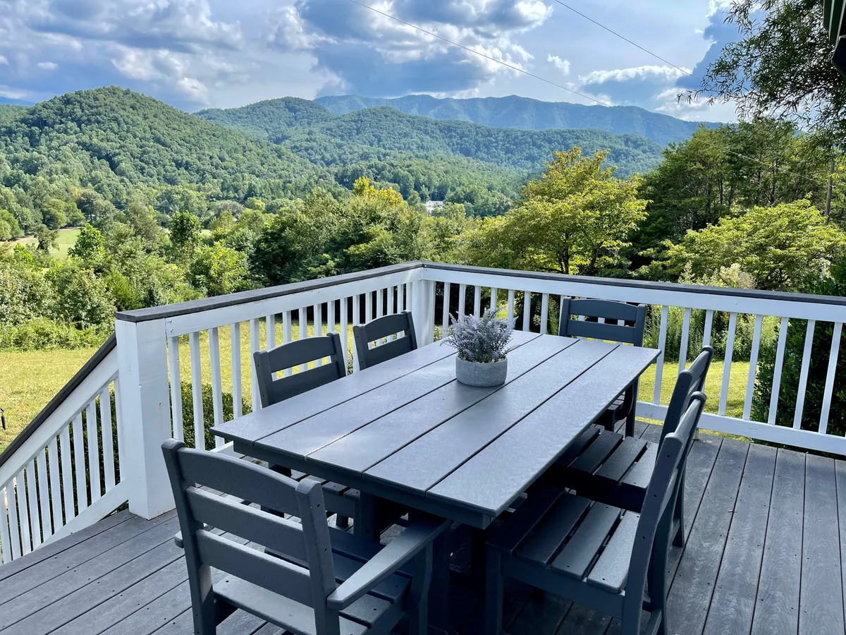 An outdoor dining table is set on a deck with sweeping mountain views and a decorative plant, creating an inviting space for relaxation or gathering after a day of hiking or exploring. The tranquil ambiance and open-air setup highlight the deck's appeal for enjoying the fresh mountain air.