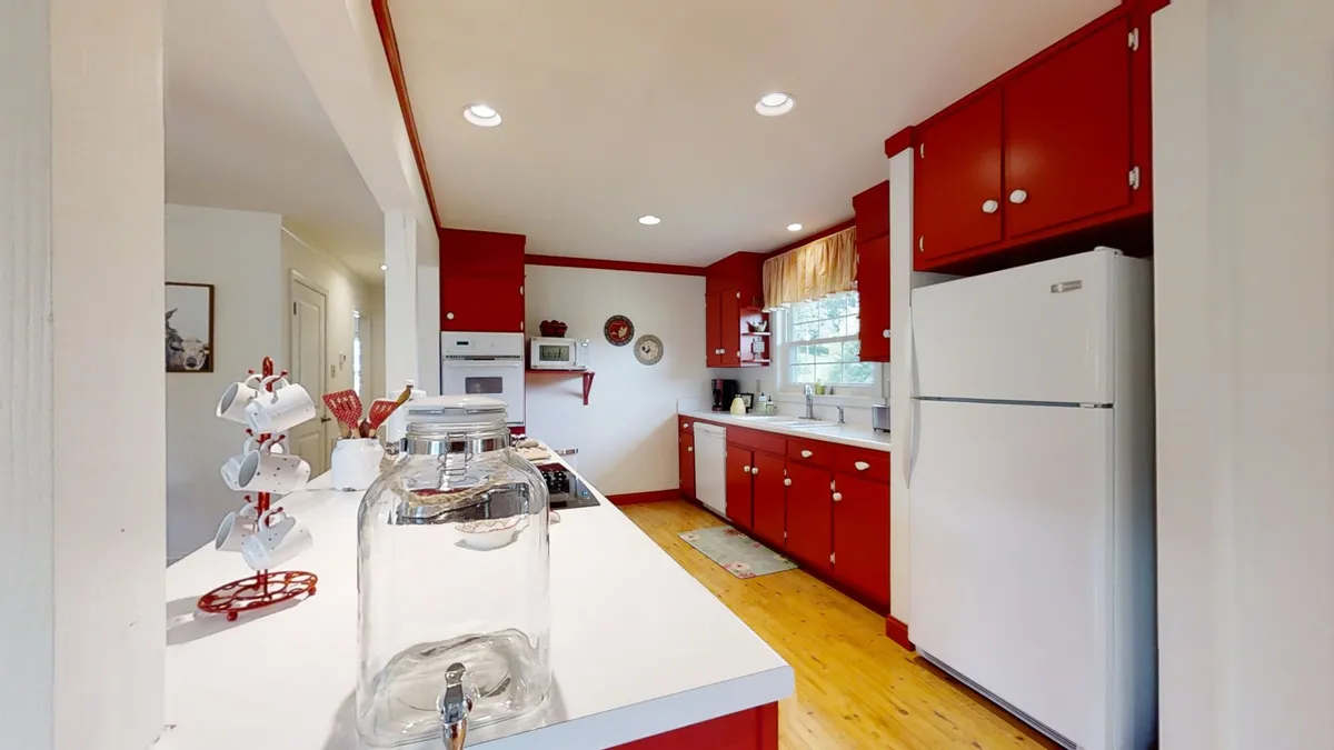 This image features a modern kitchen with striking red cabinetry and sleek white countertops. Built-in appliances and ample workspace suggest a space designed for both culinary creativity and everyday convenience. Subtle farmhouse accents and warm lighting evoke a cozy, inviting atmosphere.