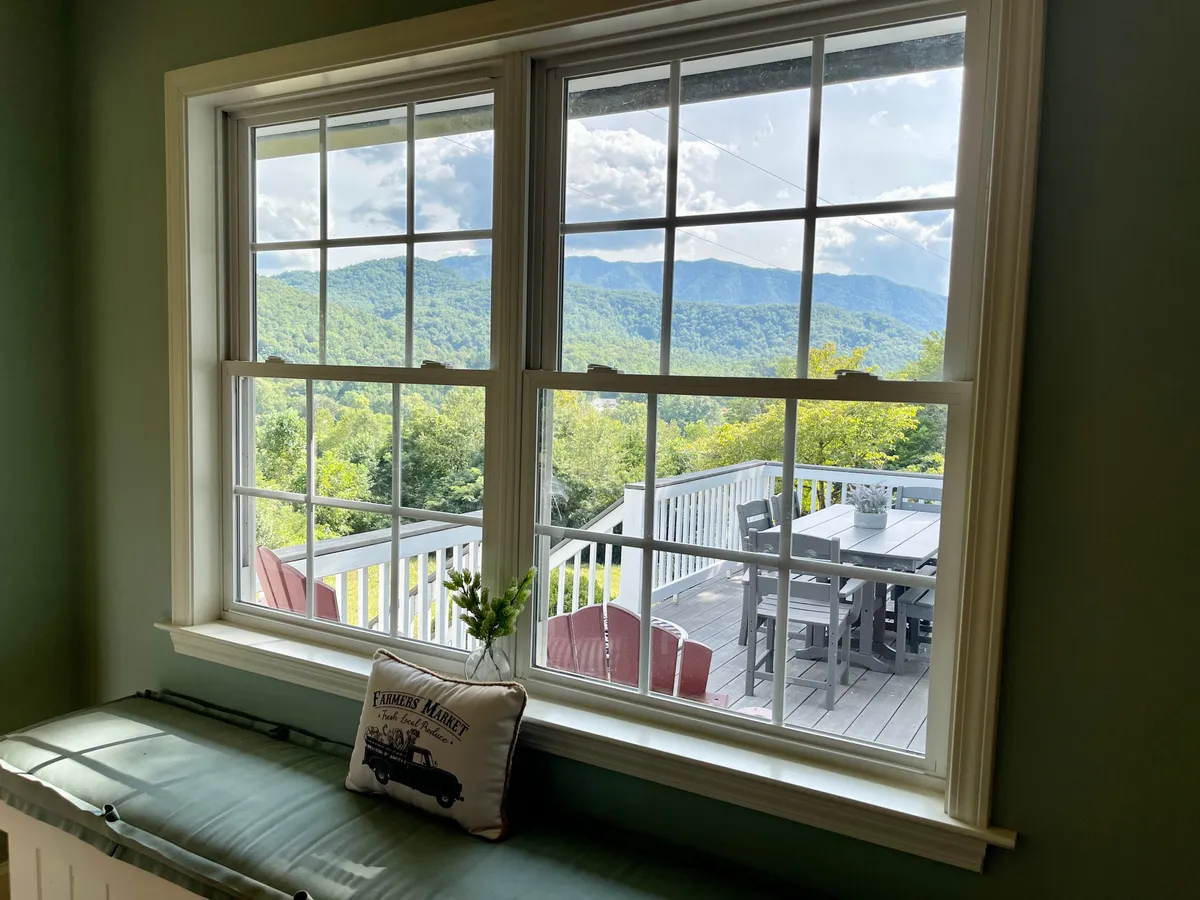 This image showcases a breathtaking mountain view from a cozy outdoor dining area. A cushioned bench and a potted plant on the window sill invite guests to relax and soak in the scenery. The serene setting is perfect for enjoying breakfast with a view or stargazing at night, with the mountains providing a romantic backdrop.