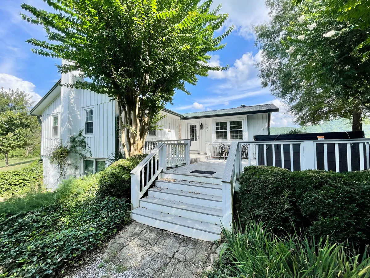 This image presents a white wooden house surrounded by lush greenery, with a welcoming patio area featuring comfortable outdoor furniture. The scene suggests a peaceful retreat, perfect for outdoor meals or relaxing together in a natural setting. The home’s exterior connects the property to its scenic Smoky Mountain context.