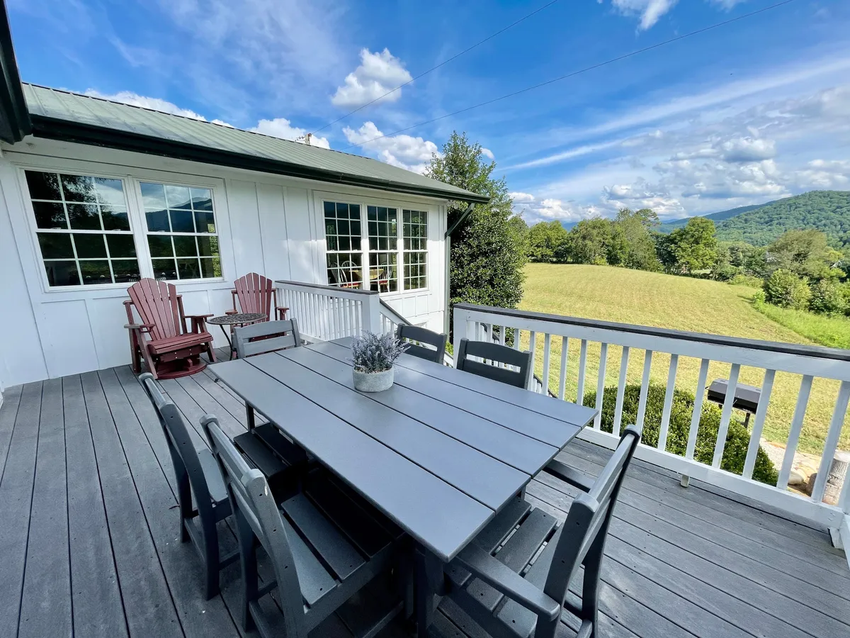 The scene shows a serene patio area featuring a dining table, a pair of Adirondack chairs, and an expansive view of open fields and mountains beyond. The setting is ideal for outdoor relaxation, shared meals, and stargazing in a tranquil mountain atmosphere.