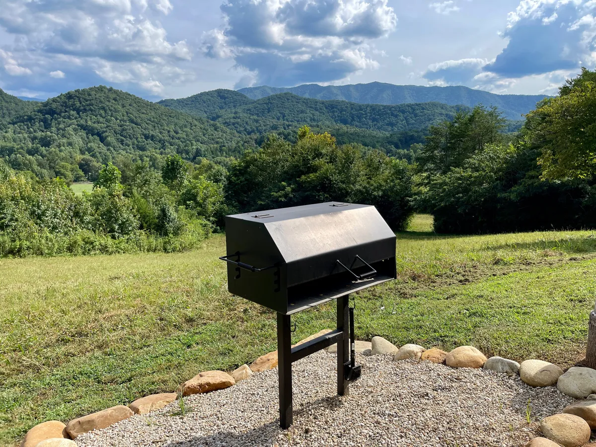 This exterior image centers on a grill set against a lush green backdrop with mountain vistas in the distance. The space is tailored for barbecuing, picnicking, and casual outdoor gatherings, making it ideal for communal meals and lively group moments.